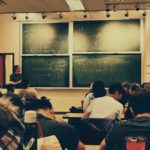 student sitting on chairs in front of chalkboard